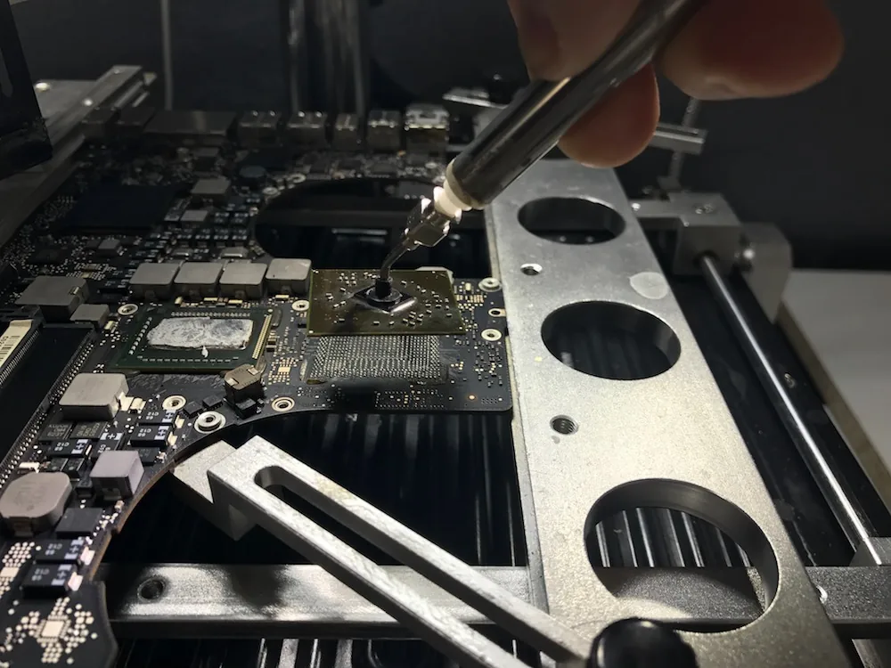 Scheda madre di un MacBook con il chip grafico in fase di sostituzione sotto la stazione di saldatura